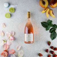 Botella de vino rosado Conti Thun Micasa con flores rosas, lima, melocotones, fresas y hojas verdes sobre fondo claro.