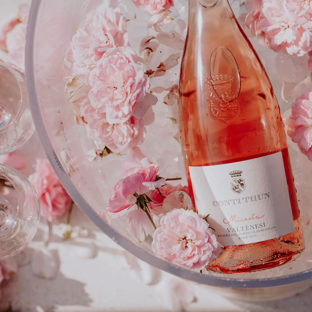 Botella de vino rosado Conti Thun Micasa con rosa rosa claro en hielo transparente y copas de vino al lado.
