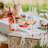 Botella de vino rosado CONTE VITUS y dos copas llenas en cesta de picnic de mimbre en ambiente exterior luminoso.