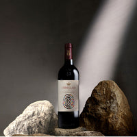 Botella de vino Ornellaia 2022 sobre un soporte de rocas, con etiqueta artística colorida y fondo gris.