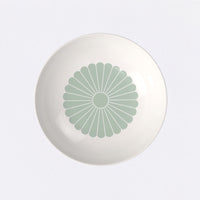 piatto rotondo di ceramica bianca con motivo centrale a forma di fiore stilizzato verde chiaro su sfondo bianco, vista dall'alto