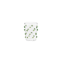 Verre transparent en verre avec petites sphères décoratives vertes incrustées sur la surface, fond blanc.