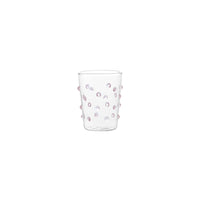 Verre transparent en verre avec décorations en relief rondes de couleur rose sur fond blanc.