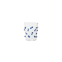 Verre transparent en verre avec décorations bleues à pois convexes distribuées sur la surface, fond blanc.
