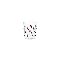 Verre transparent en verre avec petits points décoratifs rouges et noirs sur fond blanc.