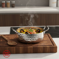 Casserole en acier martelée avec anses, contenant riz jaune, crevettes, moules et petits pois, sur planche en bois dans cuisine moderne.
