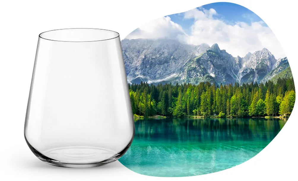 Verre transparent en verre avec forme conique inversée sur fond blanc et paysage montagneux avec lac et