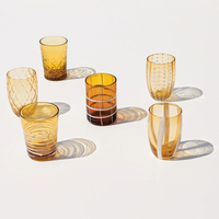 six translucent amber glass cups with various geometric decorations and patterns, on uniform white background