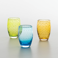 Tre bicchieri di vetro trasparente puntinati, nei colori verde, azzurro e arancione, su superficie chiara uniforme.