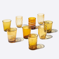 Nine amber colored glass cups with different textures and patterns on white background with soft shadows.