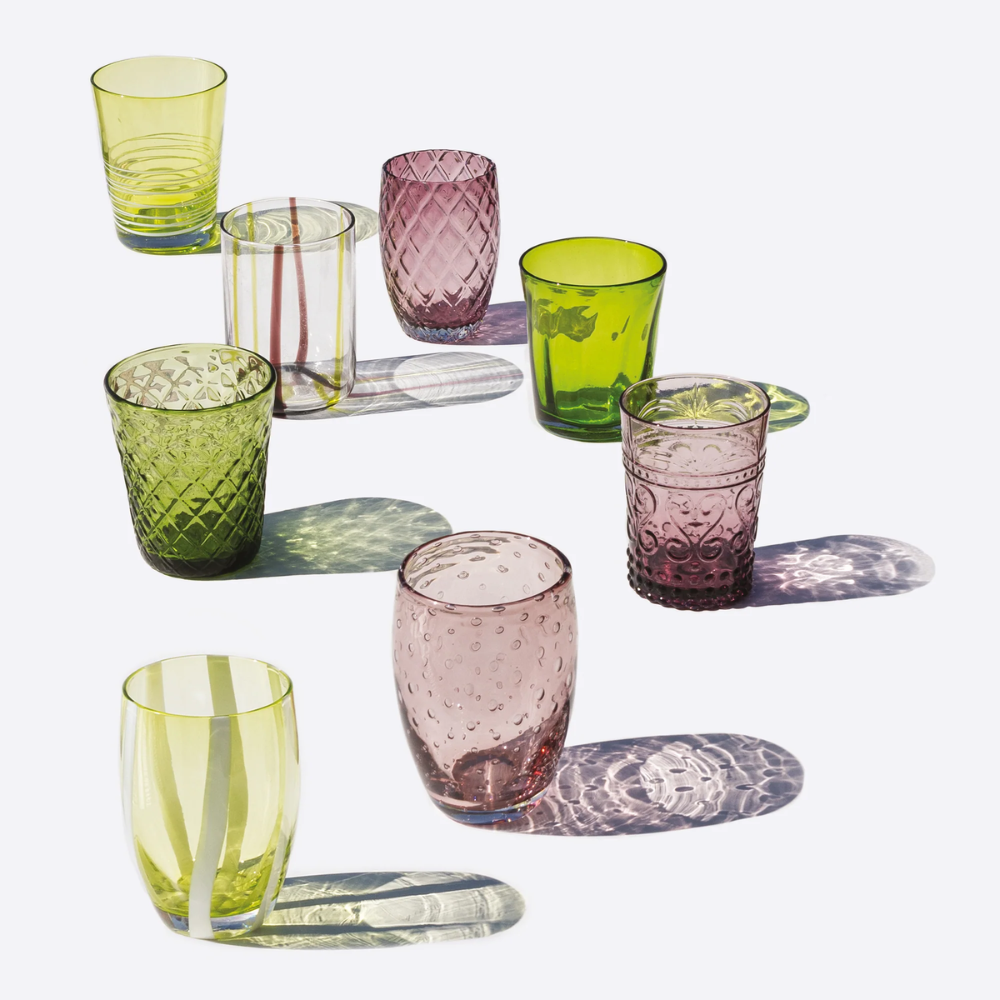 Set of eight yellow, green and pink coloured glass cups with engraved decorations, arranged on white background.