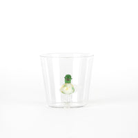 Green figurine with a smile inside a transparent glass cup, on white background.