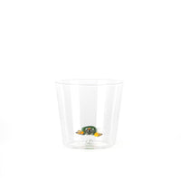 A transparent glass with a colored turtle-shaped decoration, green and yellow, positioned in the center.