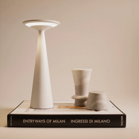 Weiße konische Lampe mit rundem Diffusor, zwei kleine Vasen aus hellem Marmor und Designbuch mit weiß-schwarzem Cover.