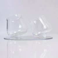 two tilted transparent glasses with rounded base on white reflective surface