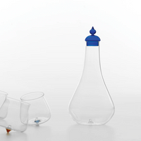 Transparent glass bottle with glossy blue cap and three tilted tasting glasses, white background.