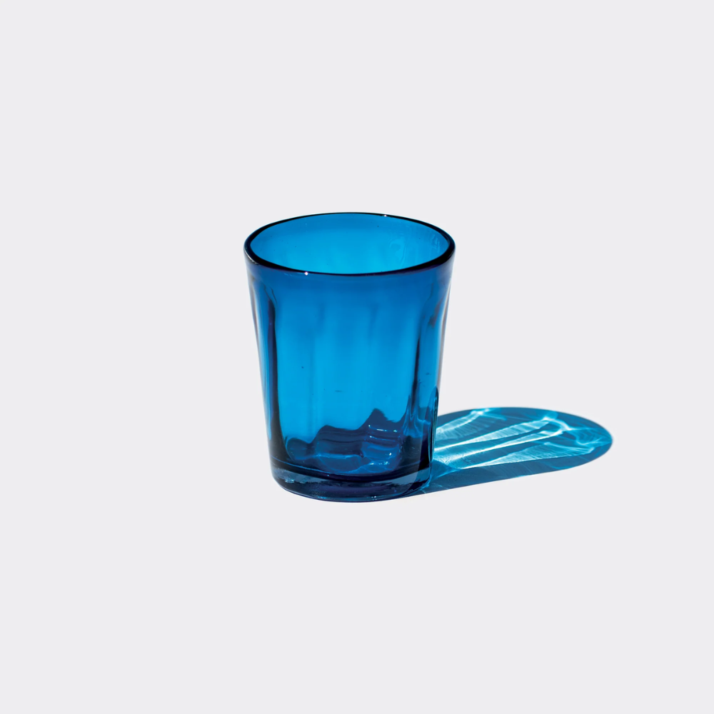 Glass tumbler blue transparent with dark rim on white background, with reflections and shadow on the right side.