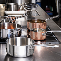 Casseroles avec manche en acier et cuivre posées sur plaque à induction dans cuisine professionnelle avec surfaces inox.
