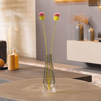 Jarrón de vidrio transparente con dos flores artificiales amarillas y rosas, sobre mesa en ambiente moderno y luminoso.