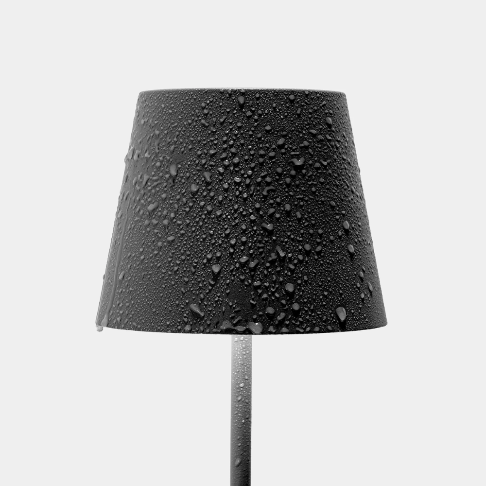 lampada da tavolo nera con paralume conico ricoperto da gocce di acqua su sfondo bianco