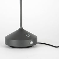 Base con stelo nero opaco, forma conica con parte superiore piatta e logo "ab+" bianco, filo nero su fondo bianco.