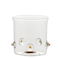 bicchiere di vetro trasparente con dettagli rotondi e piccoli elementi color ambra decorativi su sfondo bianco
