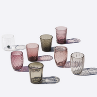 Eight transparent and colored glass cups with different textures and patterns on white surface.