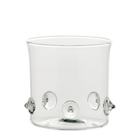Bicchiere trasparente in vetro con base cilindrica e applicazioni decorative tonde in rilievo trasparente su fondo bianco.