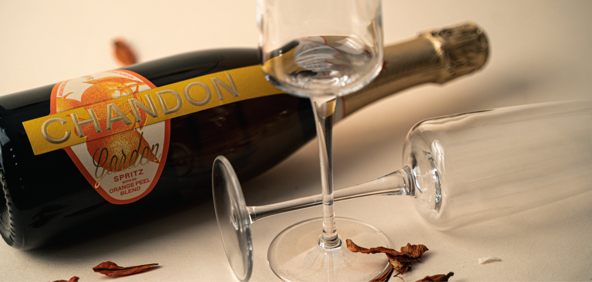 Bottiglia di vino Chandon Garden Spritz con buccia d'arancia, due calici trasparenti e petali secchi su