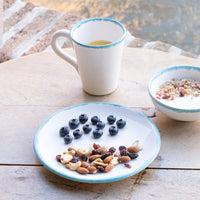 Bord met gedroogd fruit en bosbessen op houten tafel, witte kop met blauwe rand en kom yoghurt met granen.
