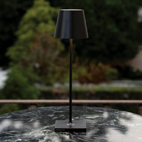 Black table lamp with conical shade and square base on green marble table outdoors, Poldina Pro lettering on base