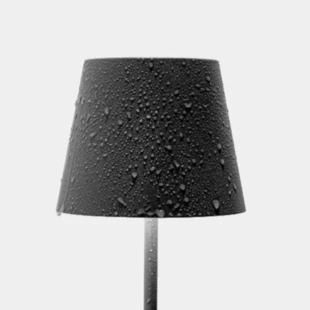 Black table lamp with bell shade and water droplets, gray cylindrical base on uniform light background