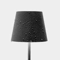 Black table lamp with bell shade and water droplets, gray cylindrical base on uniform light background