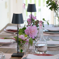 Black metal table lamp with conical shade on wood set table with pink flowers and transparent glass carafe