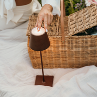 Female hand with white nails turning on a brown lamp in a setting with wicker basket and white fabrics