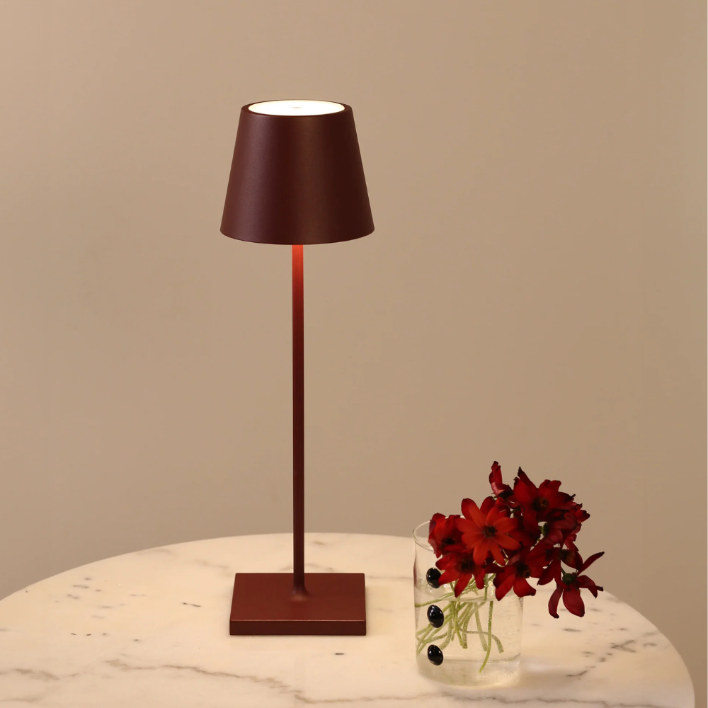 Modern brown table lamp with conical metal shade and transparent vase with red flowers on white marble table.