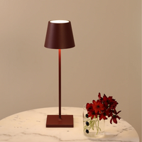 Modern brown table lamp with conical metal shade and transparent vase with red flowers on white marble table.