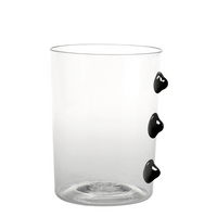 Verre transparent en verre avec trois décorations noires bombées sur le côté, fond blanc simple