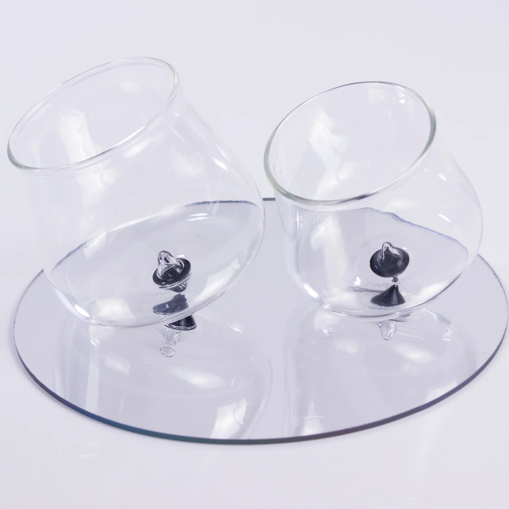 two round transparent glass glasses with black base, placed on a round transparent plate, white background