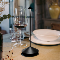 Matte black napkin holder with conical base and thin rod ending in a triangle, placed on beige tablecloth in an elegant table setting