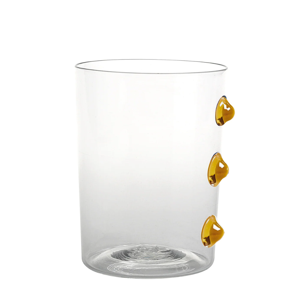Verre transparent avec trois gouttes décoratives en verre couleur ambre disposées verticalement sur un côté, fond blanc.