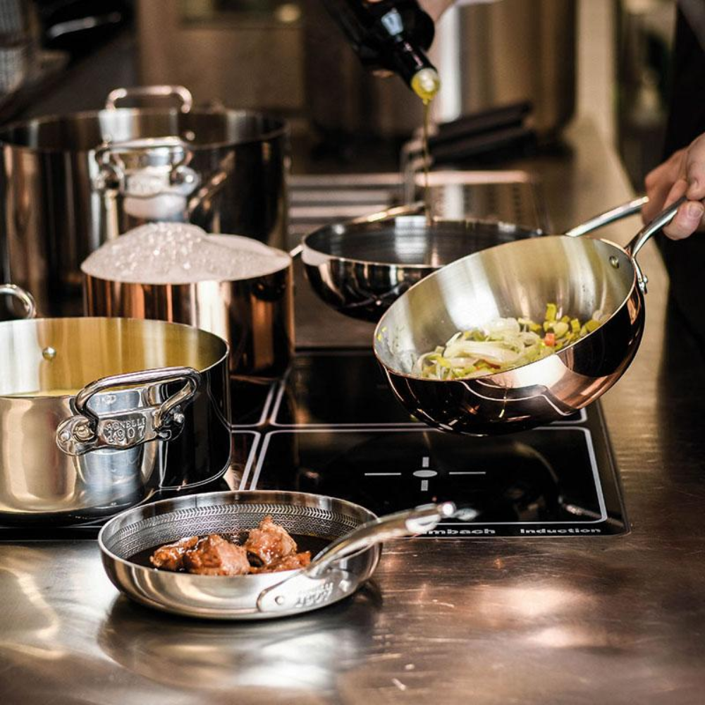 Manos vierten aceite en sartén baja acero brillante con verduras, otras ollas acero con agua hirviendo y trozos carne