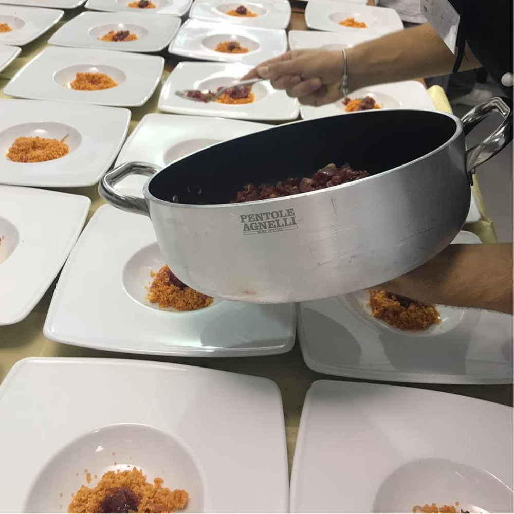 Olla de acero satinada con grabado Pentole Agnelli, usada para servir salsa roja en platos blancos con cuscús.