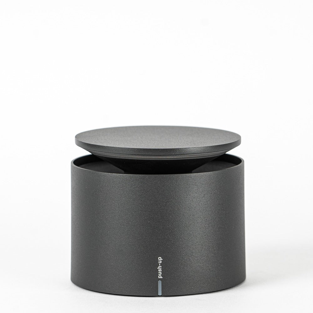 Matte black cylindrical object with flat lid, with "push-up" text on front.