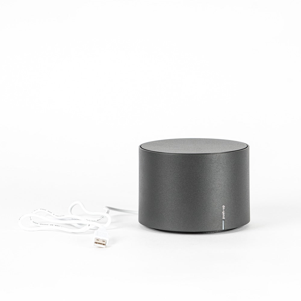 Round grey audio speaker with white USB cable, on white background.
