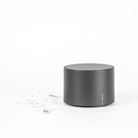 Round grey audio speaker with white USB cable, on white background.