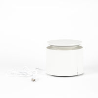 White cylindrical device with top platform, USB cable on the left on white background.
