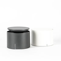 Cylindrical metal containers, one black with lid and one white, on white background.