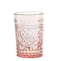 Pinkish glass tumbler with ornate raised decorations and bubble-edged base, white background