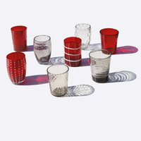 Eight transparent and red glass cups with various textures and patterns, placed on a white surface with colored shadows.